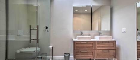 A modern bathroom with a glass shower enclosure, a white sink, and a wooden vanity.