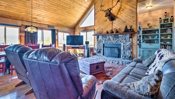 A cozy living room with leather sofas, a stone fireplace, and a mounted deer head. - Ruidoso Home w/ Hot Tub, Mtn Views & Game Room! (Ruidoso)
