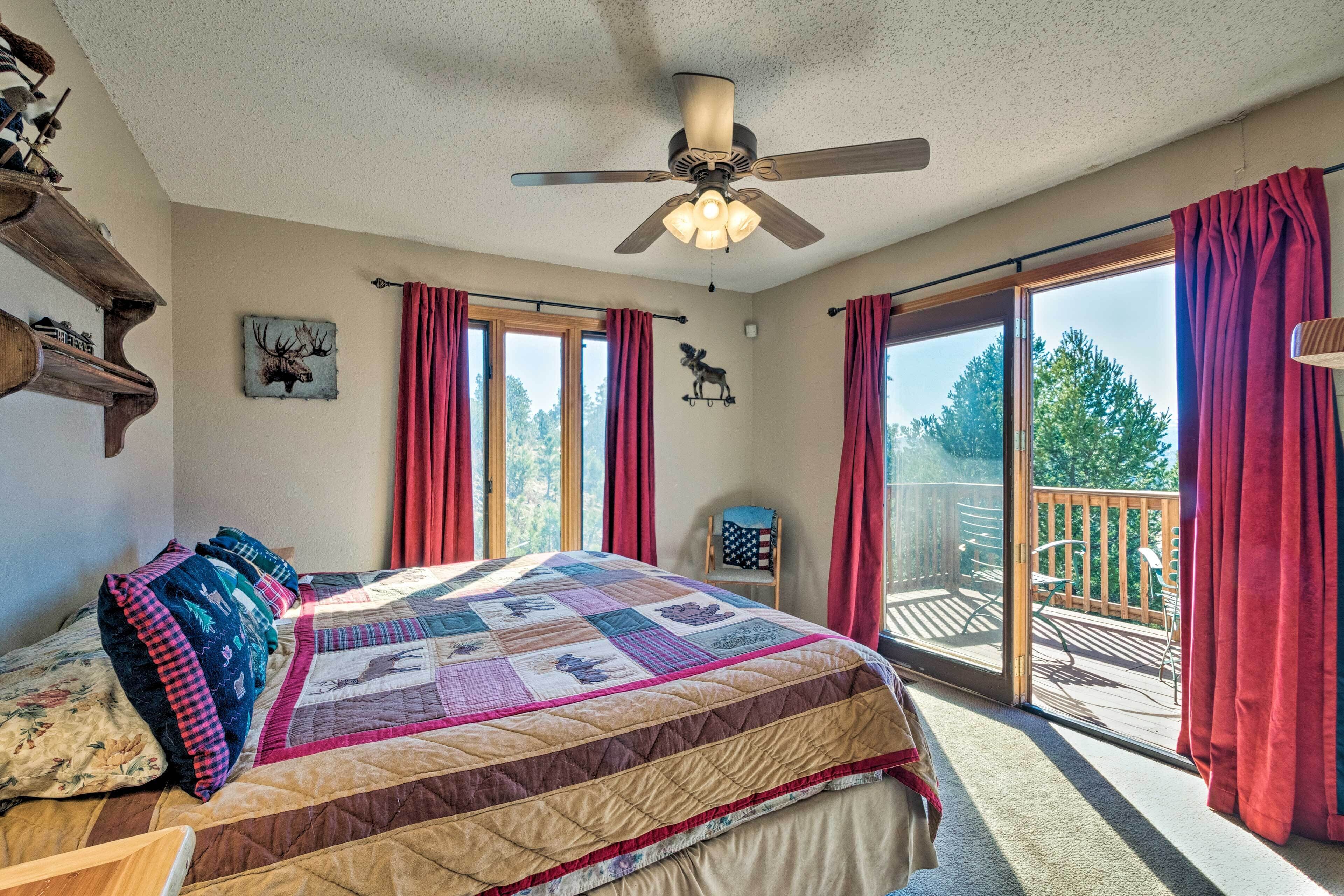 A bedroom with a large bed, a ceiling fan, and a view of the outdoor deck through a sliding glass door.