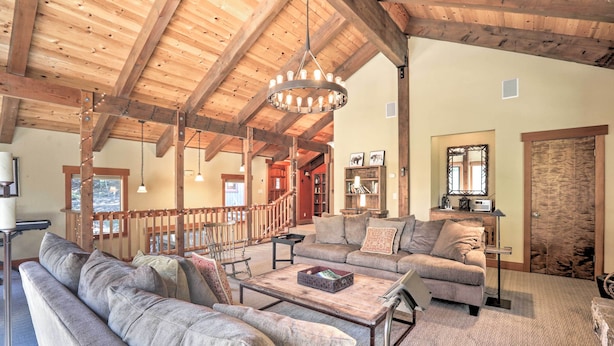 Ein geräumiges Wohnzimmer mit hoher Holzbalkendecke, einem großen Kronleuchter und einer gemütlichen Sitzecke mit Sofas und einem Couchtisch.
