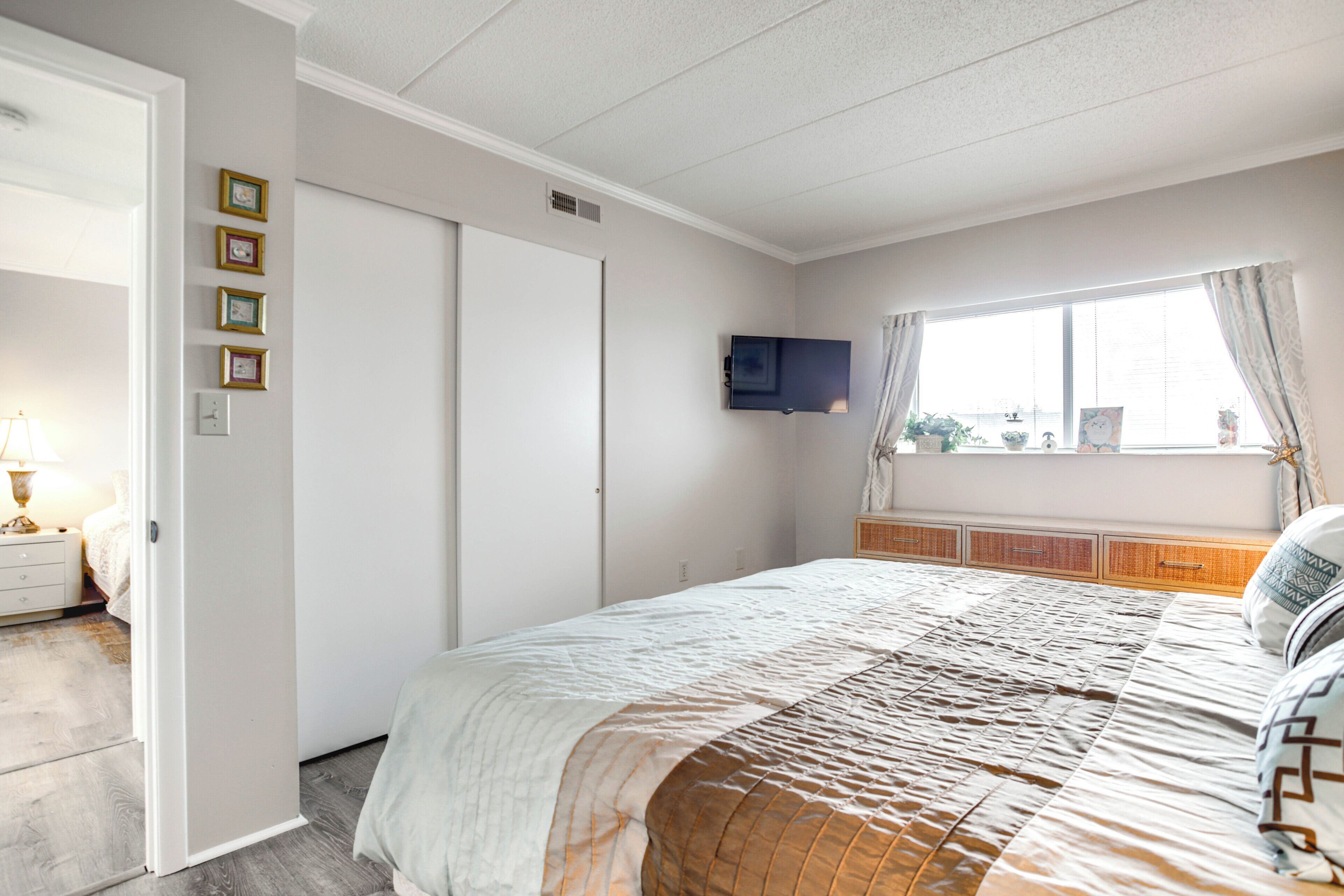 Een slaapkamer met een bed, een aan de muur bevestigde televisie, een raam met gordijnen en een nachtkastje met een lamp.