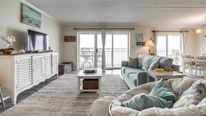 Een ruime woonkamer met een bank, een salontafel en een televisie op een kast. Er is een balkon met uitzicht op de omgeving.