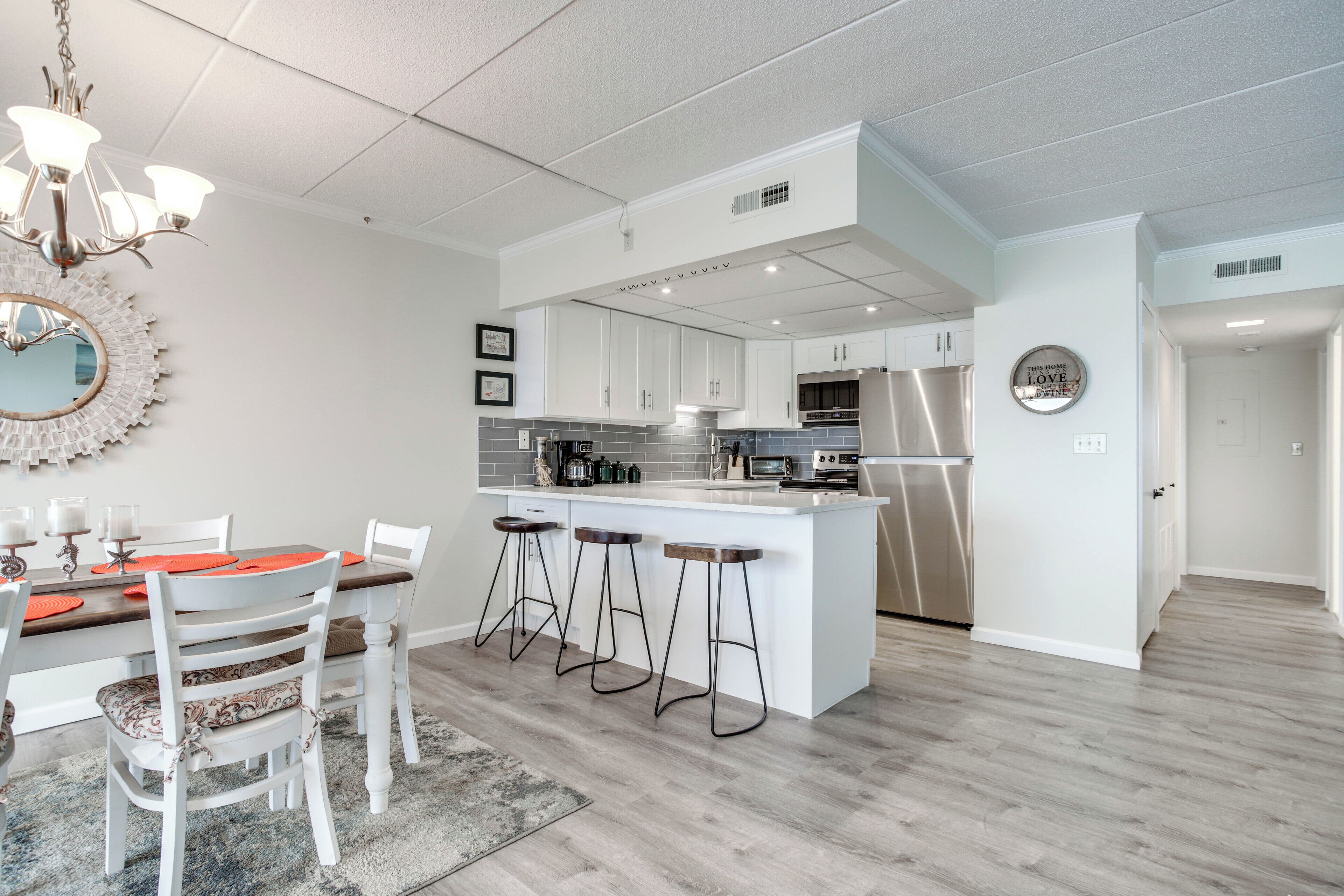 A modern kitchen with white cabinets, a central island with bar stools, and a chandelier.