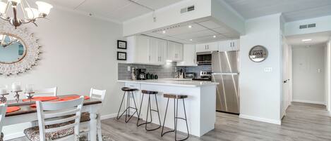 A modern kitchen with white cabinets, a central island with bar stools, and a chandelier.