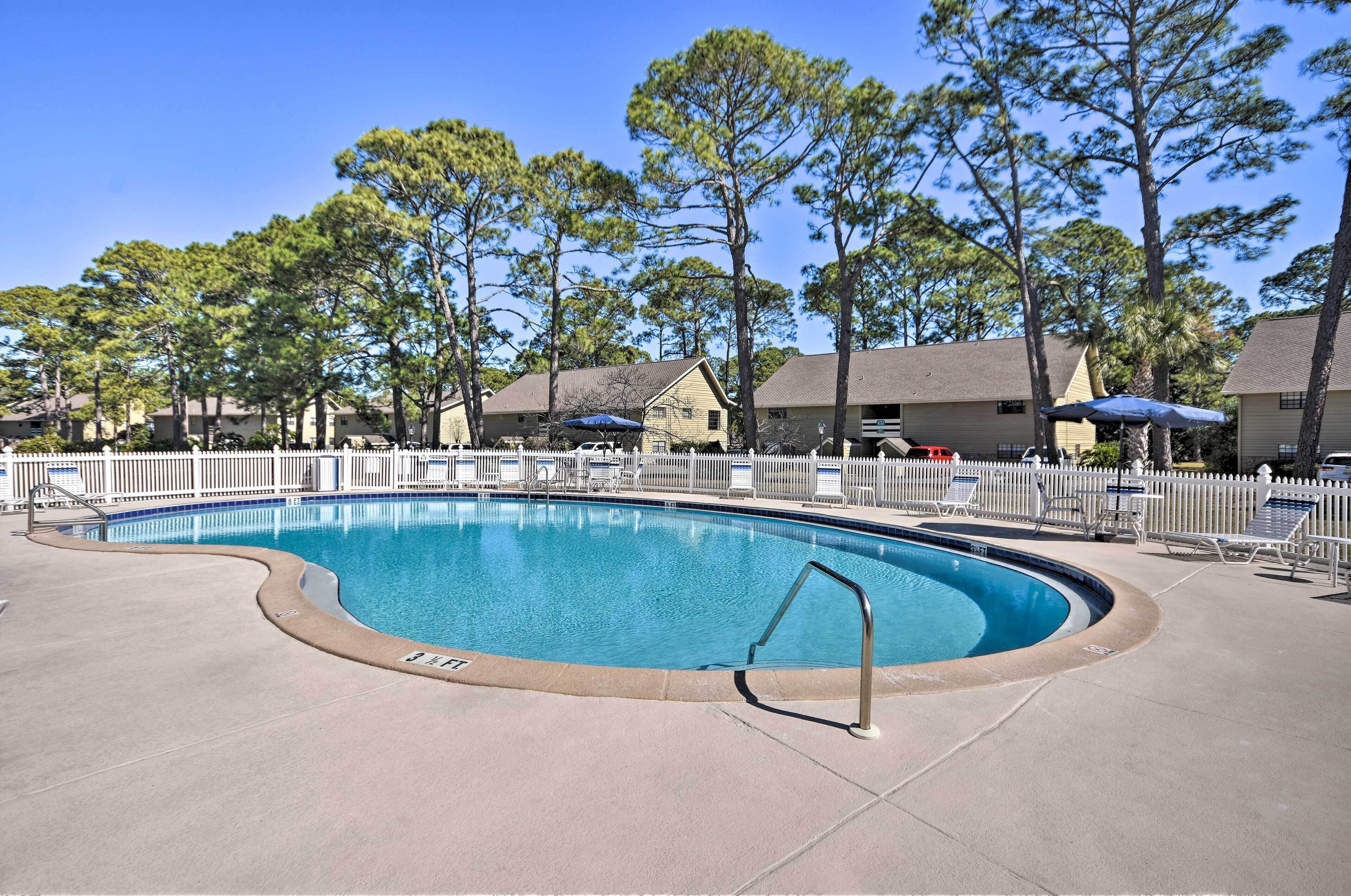 A swimming pool with a curved edge, surrounded by a white fence and lounge chairs.