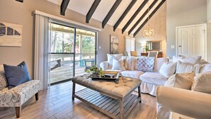 Un salon moderne avec un plafond en bois, une porte-fenêtre coulissante donnant sur un balcon, un ensemble de canapés blancs et une table basse avec un plateau.