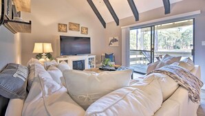 Un salon chaleureux avec une grande fenêtre, un ventilateur de plafond, un téléviseur à écran plat et un canapé confortable.