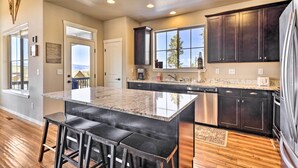 A modern kitchen with a large island, dark cabinets, stainless steel appliances, and a view through the window. - Ski-in/out Granby Home w/ Gas Grill & Fire Pit! (Granby)