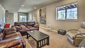A spacious living room with leather sofas, a wooden coffee table, and large windows offering a view of trees. - Ski-in/out Granby Home w/ Gas Grill & Fire Pit! (Granby)