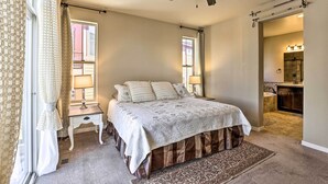A bedroom with a bed, a ceiling fan, a nightstand, a lamp, and a view of the bathroom. - Ski-in/out Granby Home w/ Gas Grill & Fire Pit! (Granby)