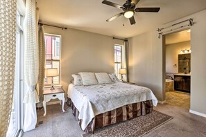 A bedroom with a bed, a ceiling fan, a nightstand, a lamp, and a view of the bathroom.