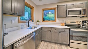 A modern kitchen with stainless steel appliances, a dishwasher, and wooden cabinets. - Custom-built Lakefront Cottage w/ Spacious Yard! (Westford)