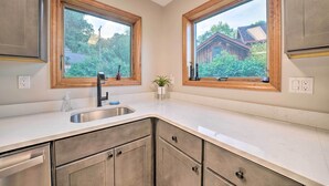 A kitchen with two windows, a stainless steel sink, and wooden cabinets. - Custom-built Lakefront Cottage w/ Spacious Yard! (Westford)