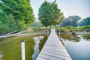 A wooden dock extending over a calm body of water, surrounded by lush greenery and trees.