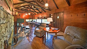A rustic wooden interior with a stone wall, wooden beams, a wooden dining table, a sofa, and a television. - Custom-built Lakefront Cottage w/ Spacious Yard! (Westford)