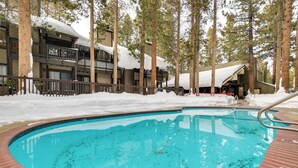 A pool area with a brick border, surrounded by tall trees and a building with balconies. - Mammoth Lakes Condo ~ 5 Mi to Mammoth Mtn! (Mammoth Lakes)