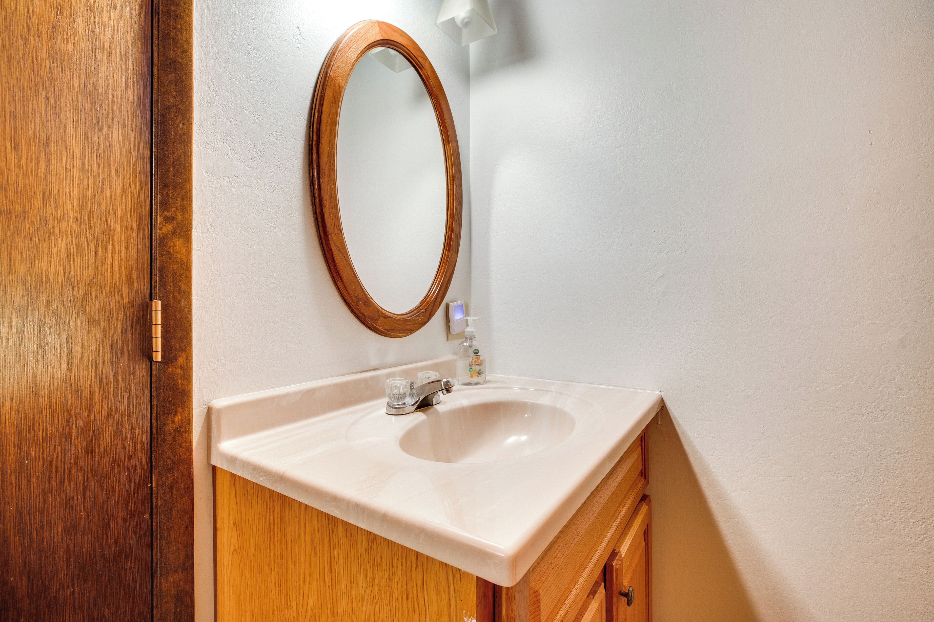 A bathroom with a wooden door, a white sink, a mirror, and a soap dispenser.