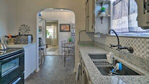 A kitchen with a stone floor, a built-in oven, a sink with a window, and a dining area with a chair and table. - El Paso Home w/ Backyard + Outdoor Fireplace! (El Paso)
