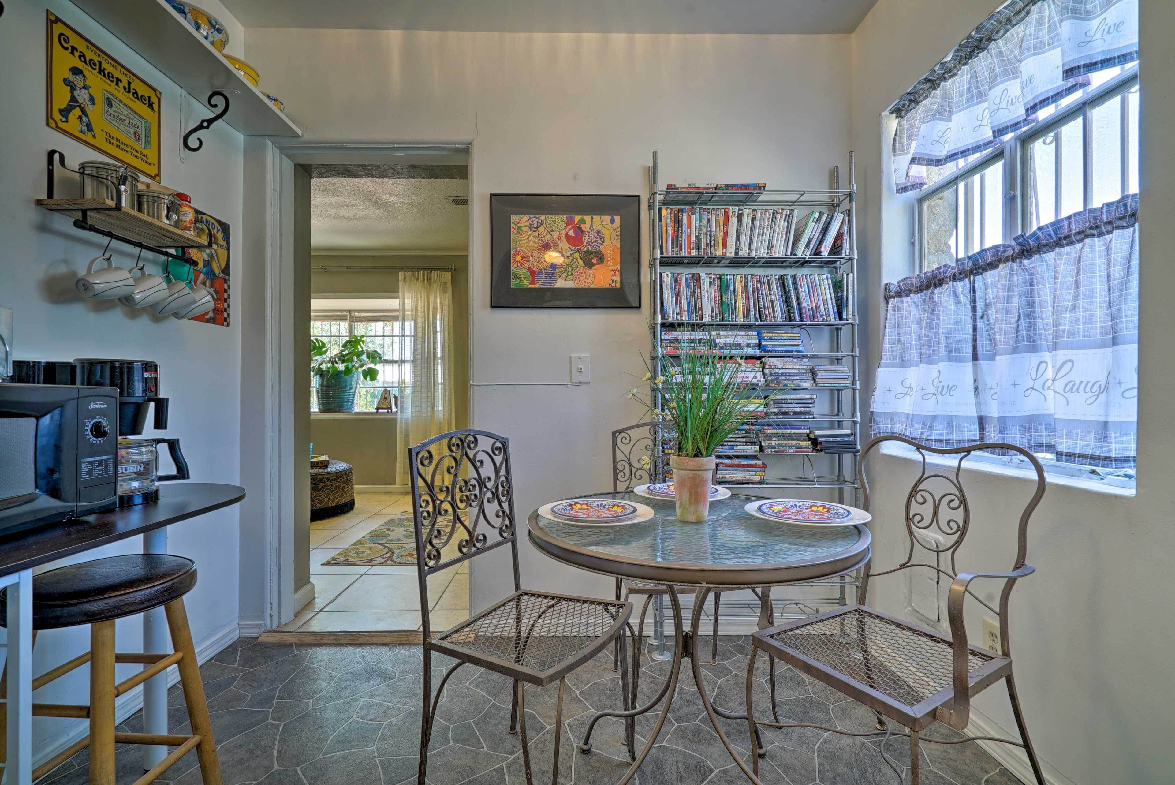 A dining area with a round table, metal chairs, a coffee machine, and a bookshelf filled with books.