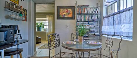 A dining area with a round table, metal chairs, a coffee machine, and a bookshelf filled with books.