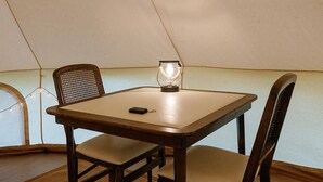 A tent with a table and four chairs, a glass on the table, and a string of lights.