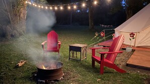 A campsite with a fire pit, two red Adirondack chairs, a small table, and a tent.