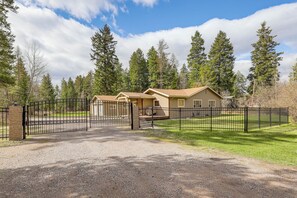 A gated residential area with two houses, a gravel driveway, and a forested background. - Columbia Falls Private Retreat: Pool Table & Deck! (Columbia Falls)