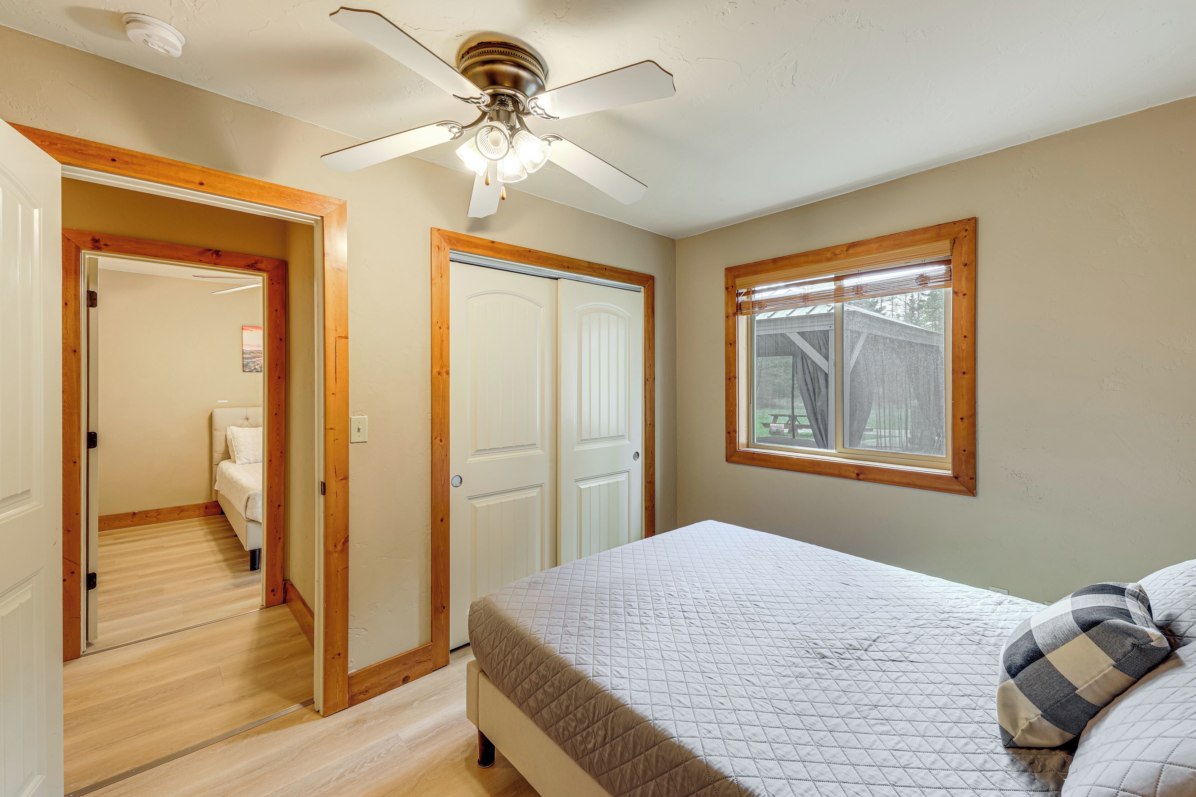 Quarto com cama, ventilador de teto, janela e porta que dá para outro cômodo.