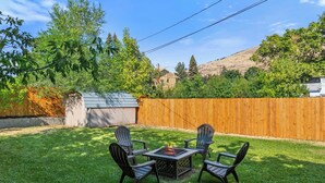 Un patio trasero con una mesa de fogata y cuatro sillas Adirondack.
