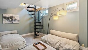 Un dormitorio con escalera en espiral, dos almohadas grandes, una mesita de noche con bandeja y una lámpara de pie.