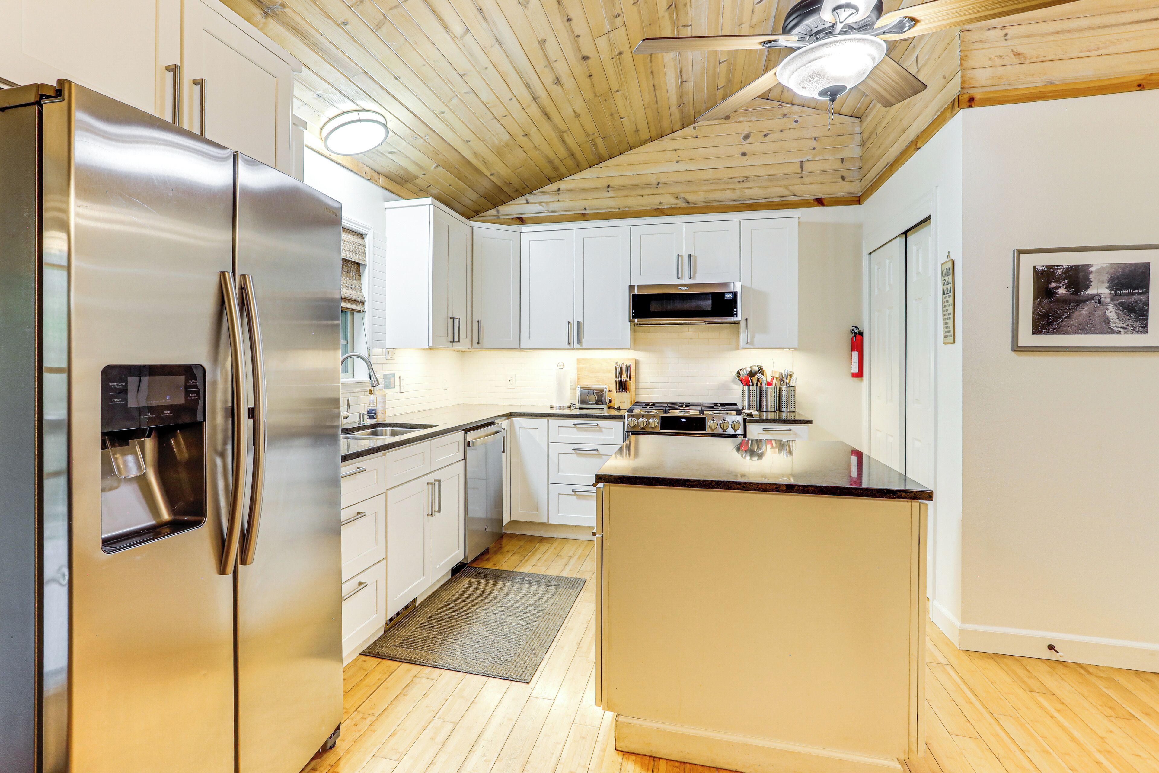 A modern kitchen with stainless steel appliances, white cabinetry, and a wooden ceiling.