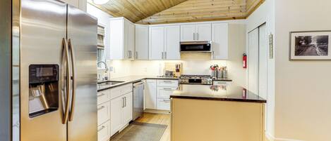 A modern kitchen with stainless steel appliances, white cabinetry, and a wooden ceiling.