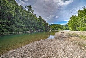A riverbank with clear water, surrounded by dense green forest and rocky terrain. - 'creekside Hideaway' w/ Fire Pit + Creek Access! (Mountain View)