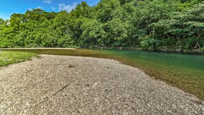 A riverbank with clear water, surrounded by dense green foliage and a rocky terrain. - 'creekside Hideaway' w/ Fire Pit + Creek Access! (Mountain View)