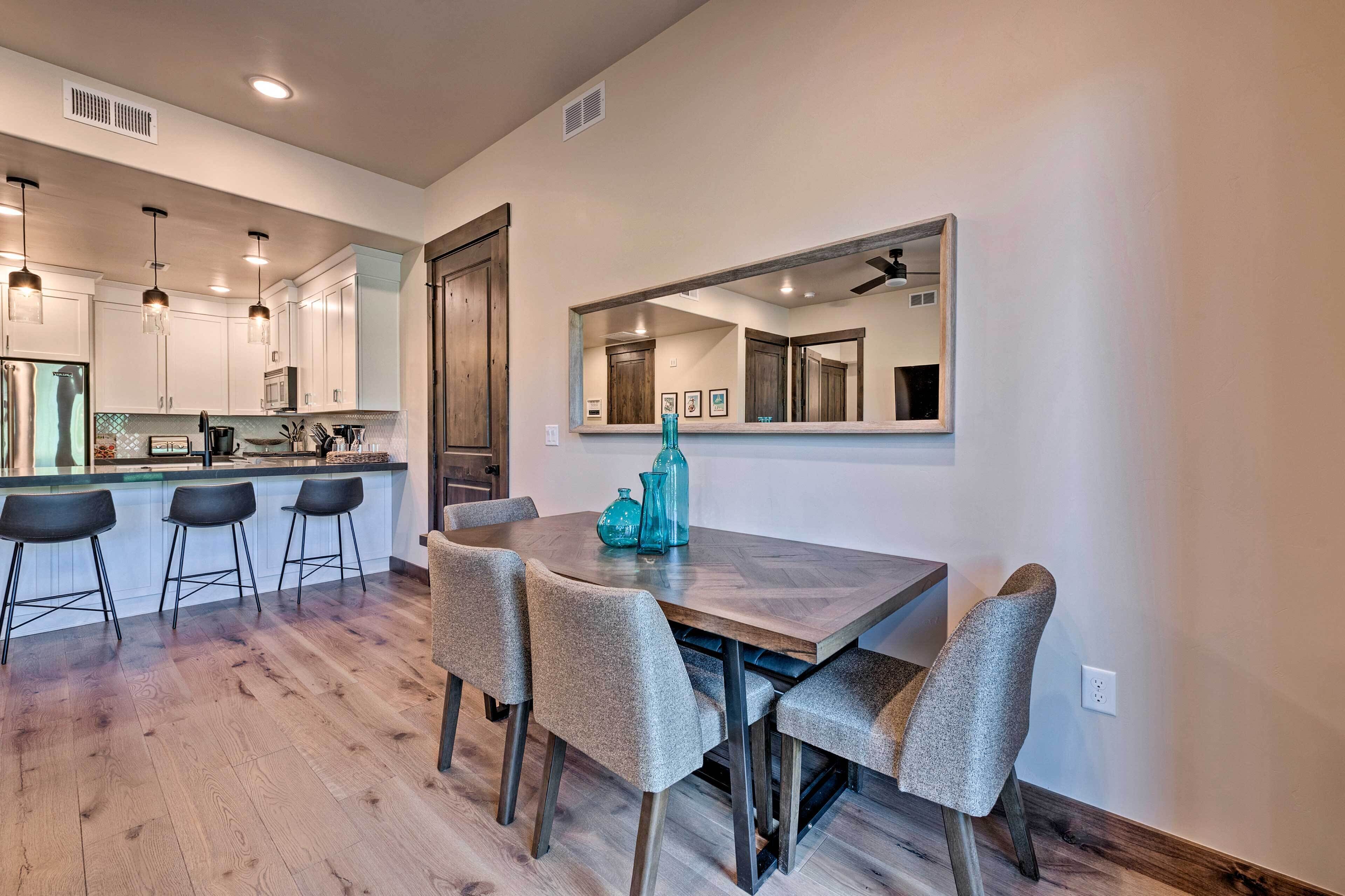 A modern kitchen with a wooden dining table, bar stools, and a large mirror above the table.