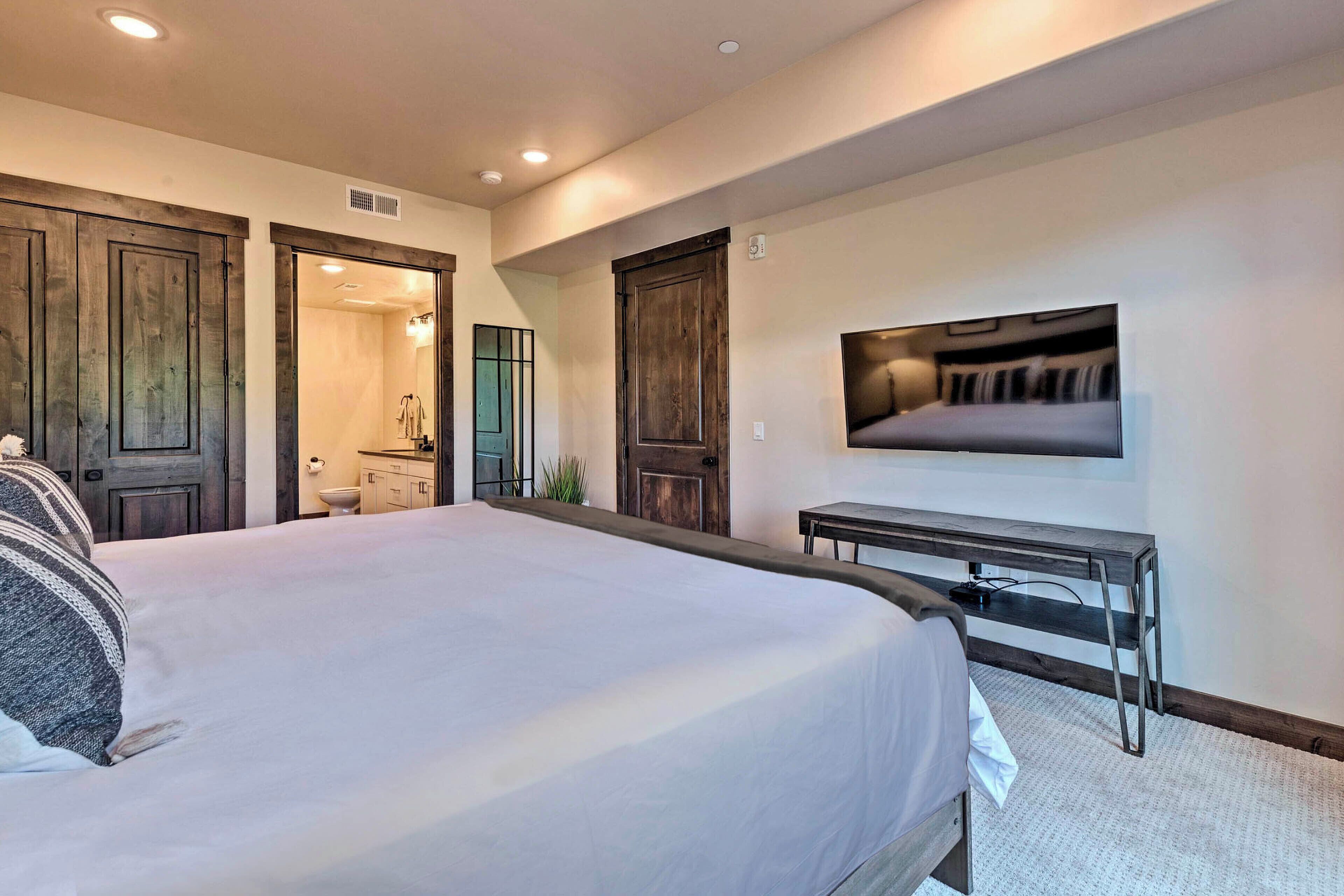 A bedroom with a large bed, a desk, and a TV mounted on the wall.