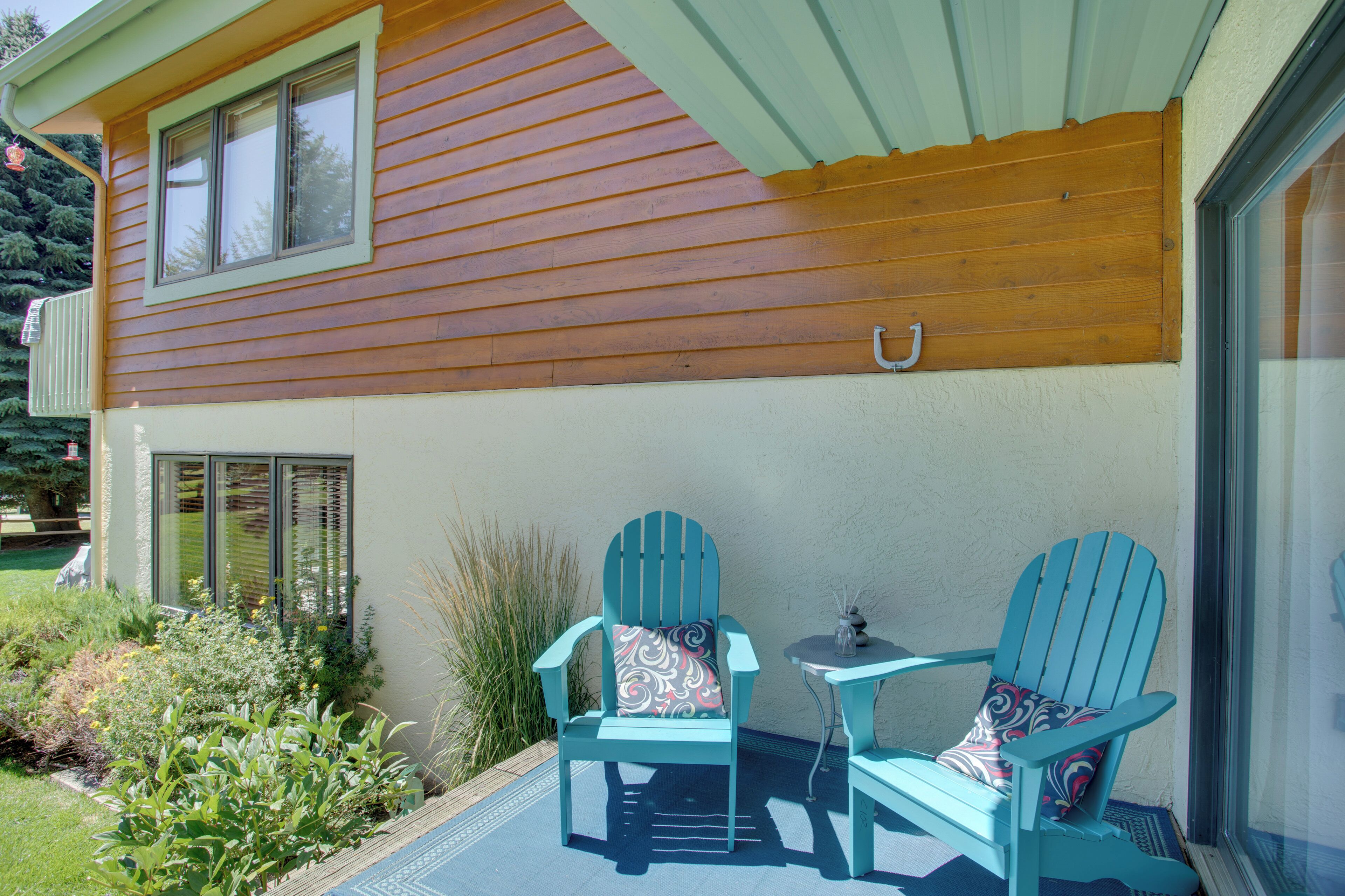 A patio with two turquoise Adirondack chairs, a small table, and a window overlooking a garden.