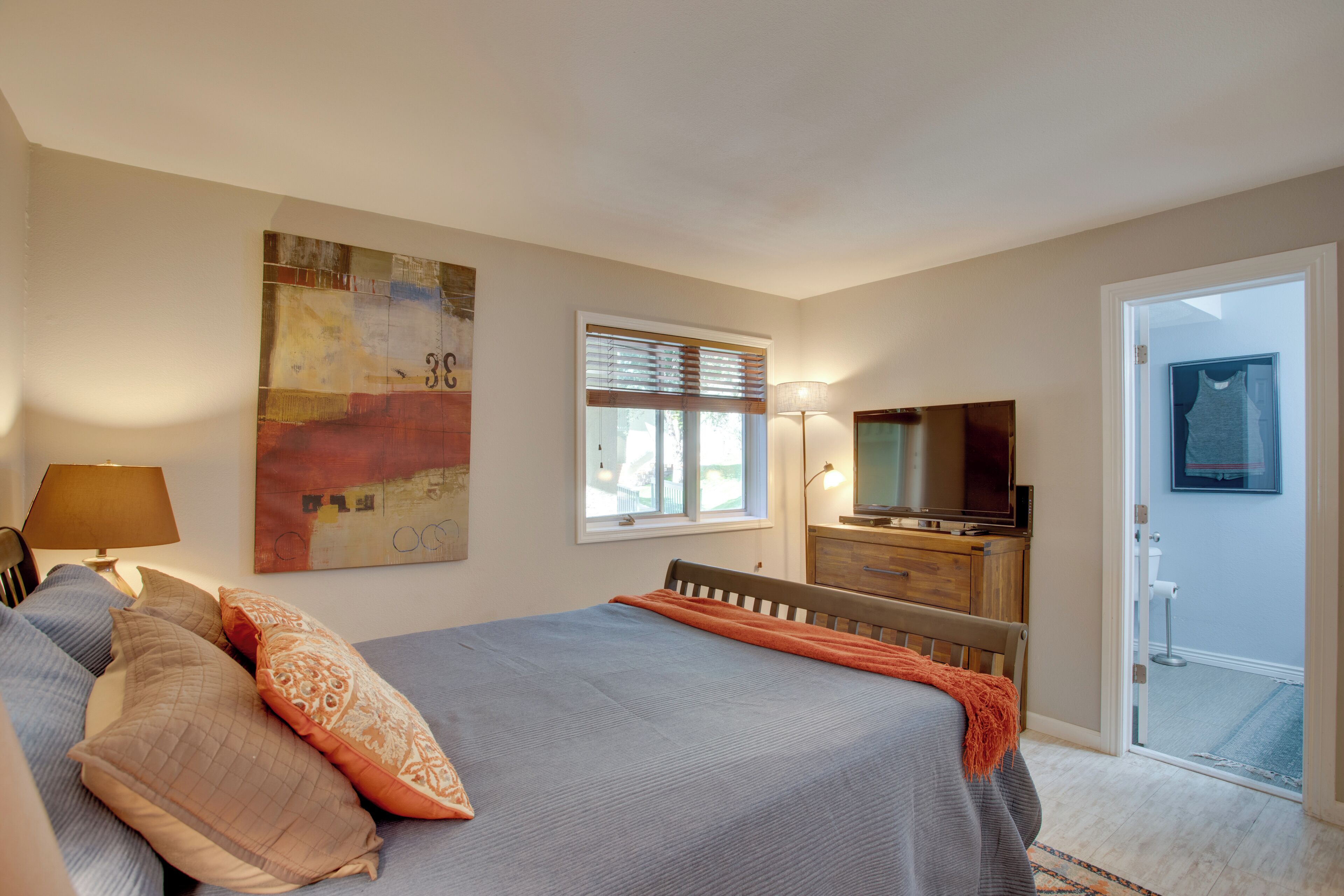 A bedroom with a bed, a TV, a dresser, a window, and a door leading to an outdoor area.