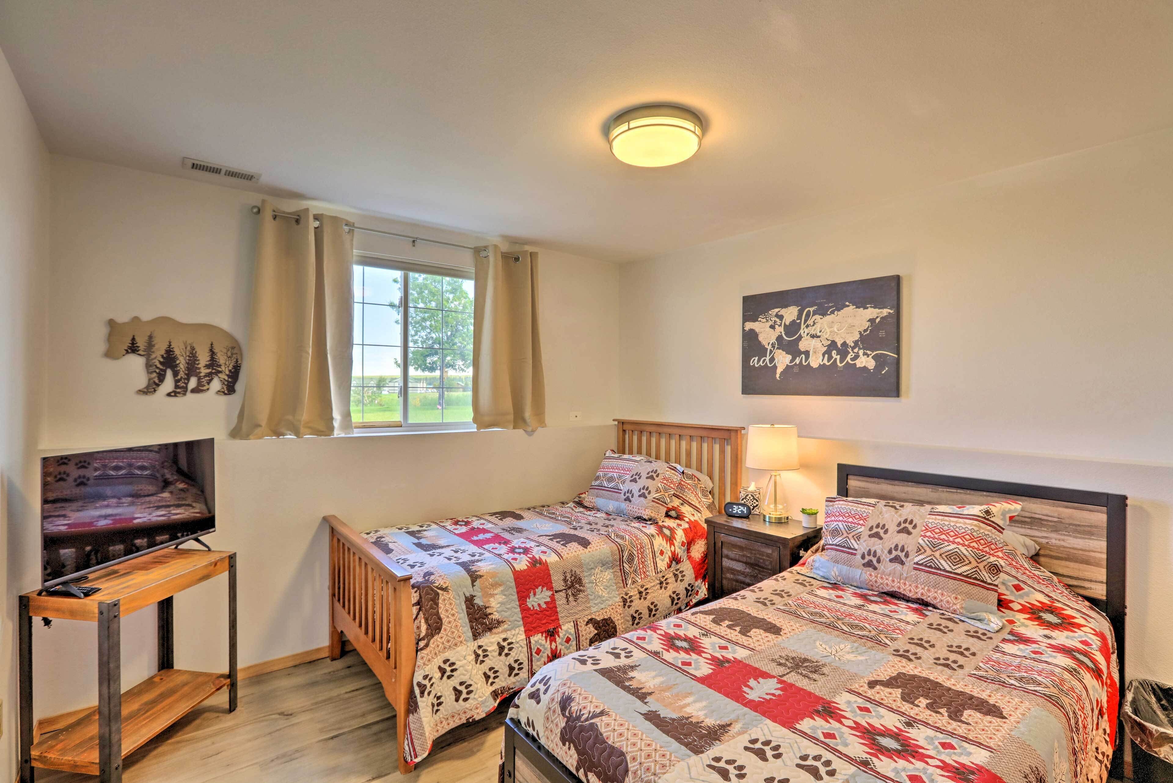 A room with two beds, a TV, a wooden table, a window with curtains, a world map on the wall, and a bear decoration.
