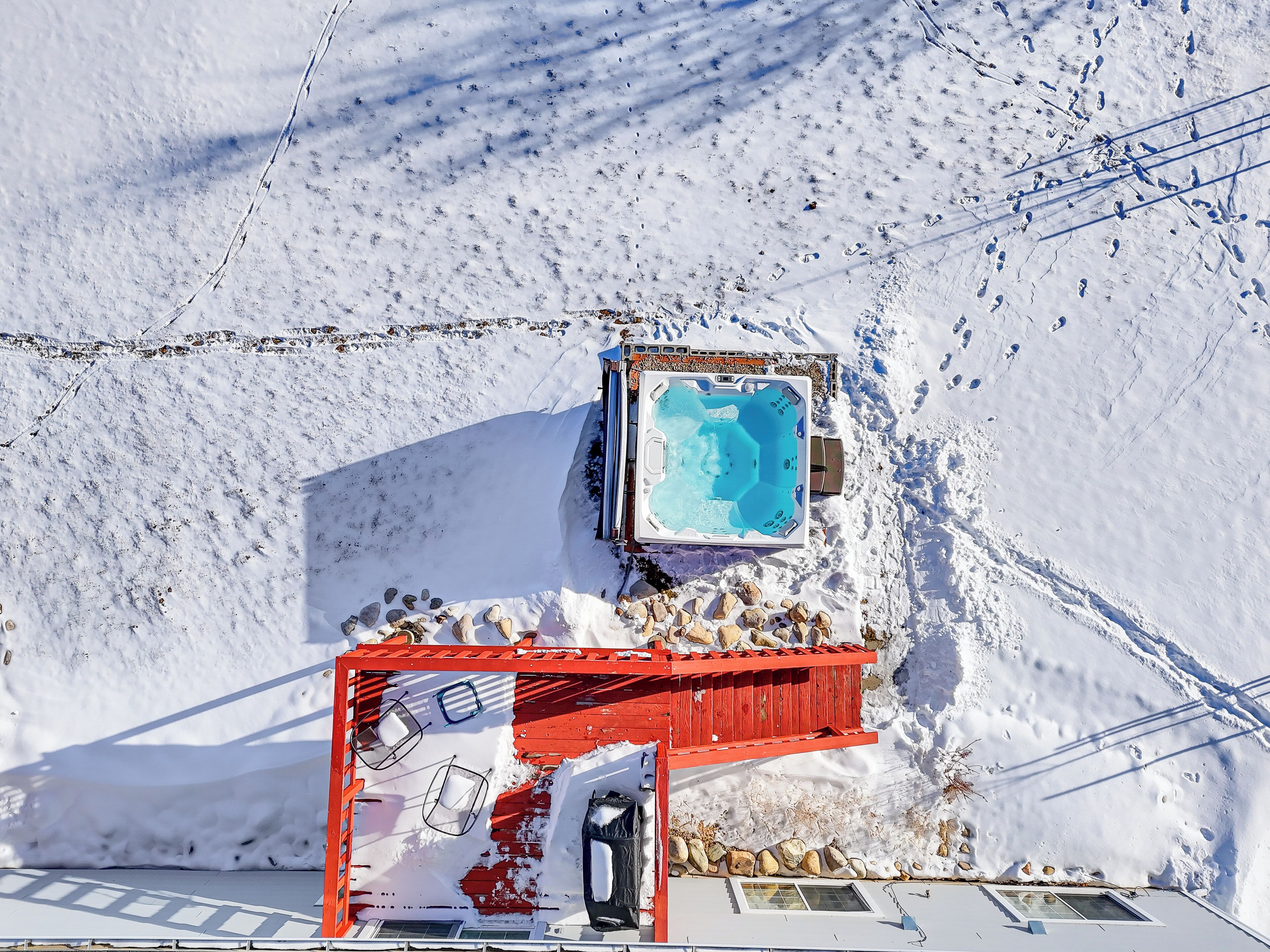 A hot tub in a snowy outdoor setting with a red wooden structure nearby.