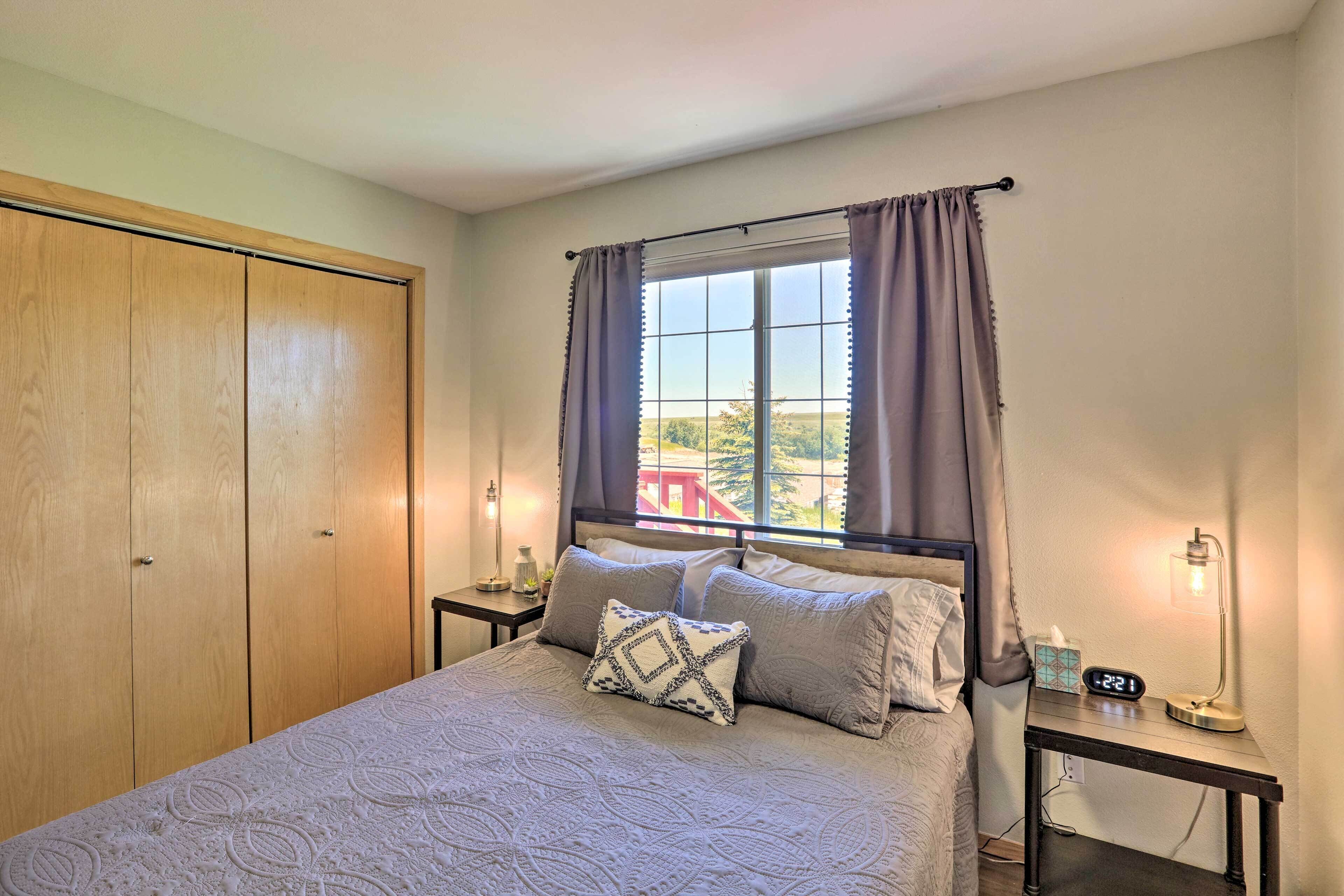 Une chambre à coucher avec un lit, une table de chevet avec une lampe, une fenêtre avec des rideaux et une armoire.