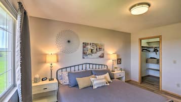 A bedroom with a bed, two bedside tables, a nightstand, a wall clock, a mirror, and a window with curtains.