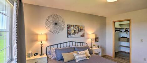 A bedroom with a bed, two bedside tables, a nightstand, a wall clock, a mirror, and a window with curtains.