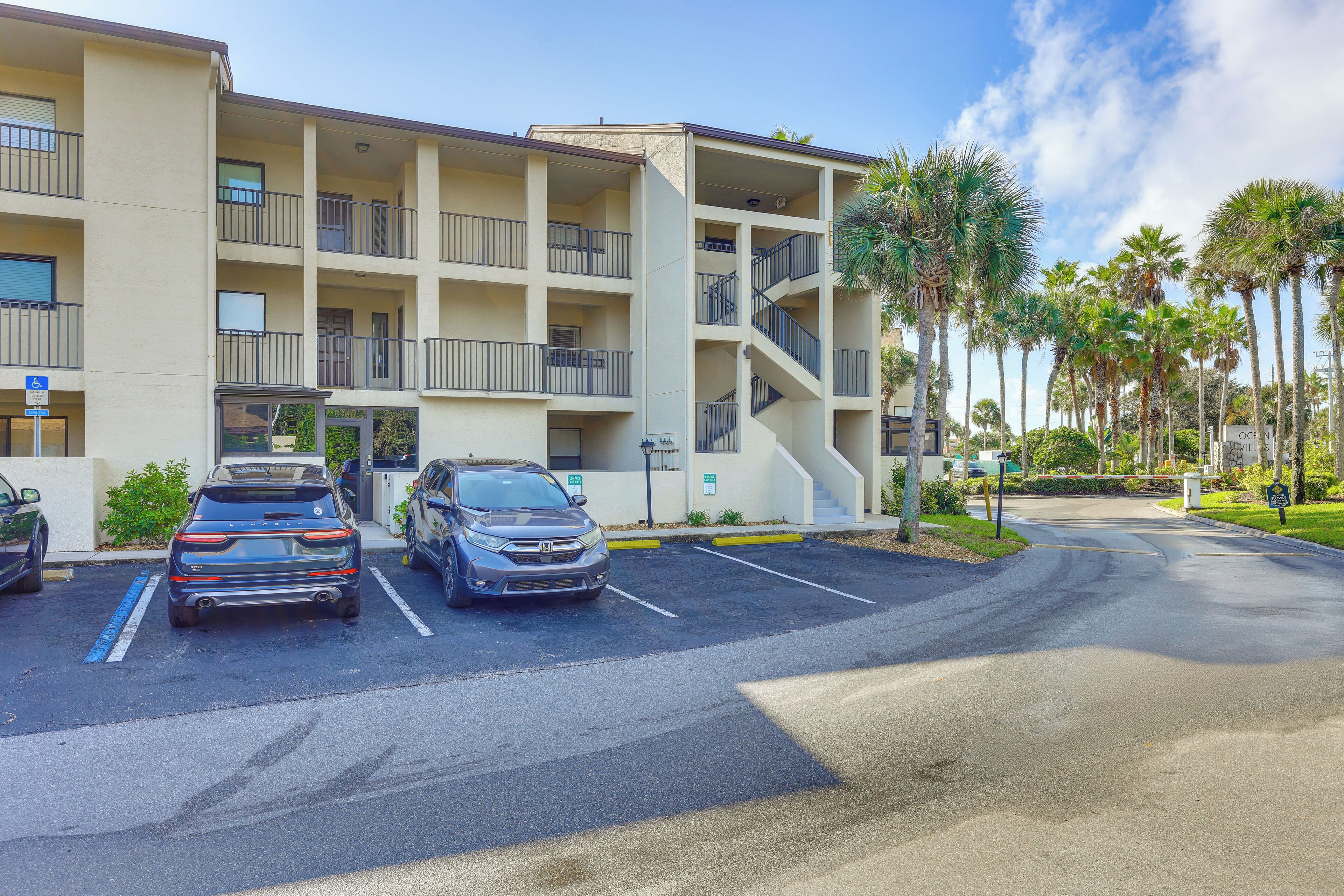 A multi-story hotel with a parking lot, palm trees, and a clear sky.