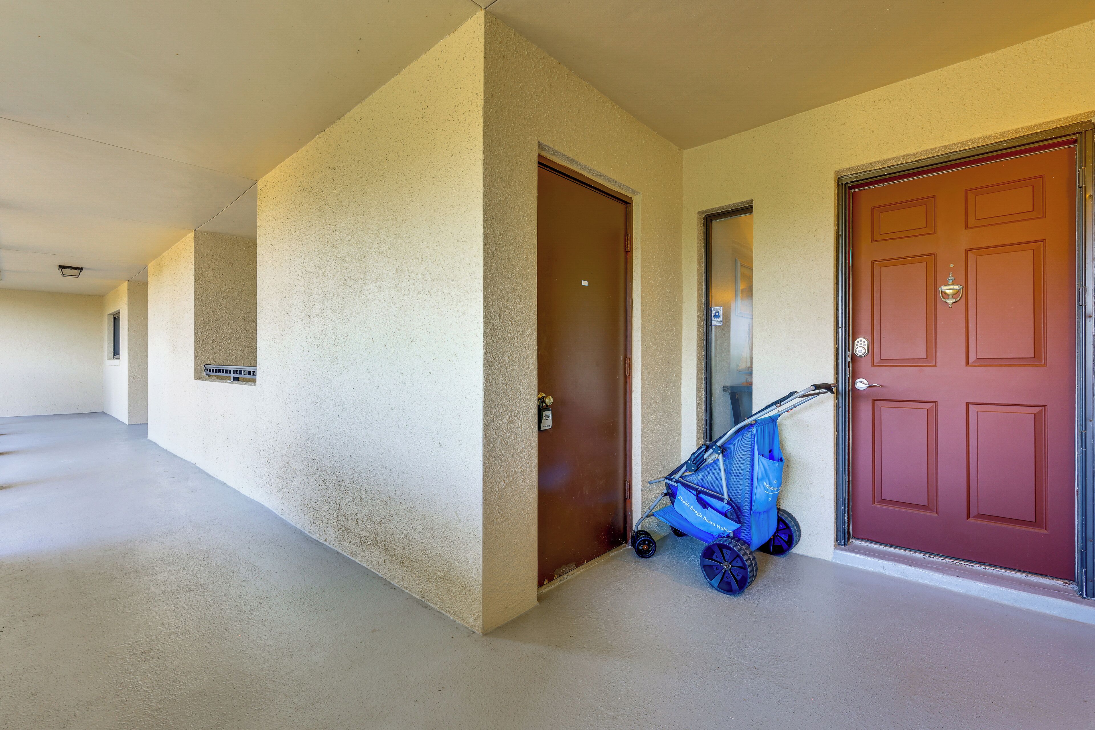 A hallway with a brown door, a red door, and a blue stroller parked by the red door.