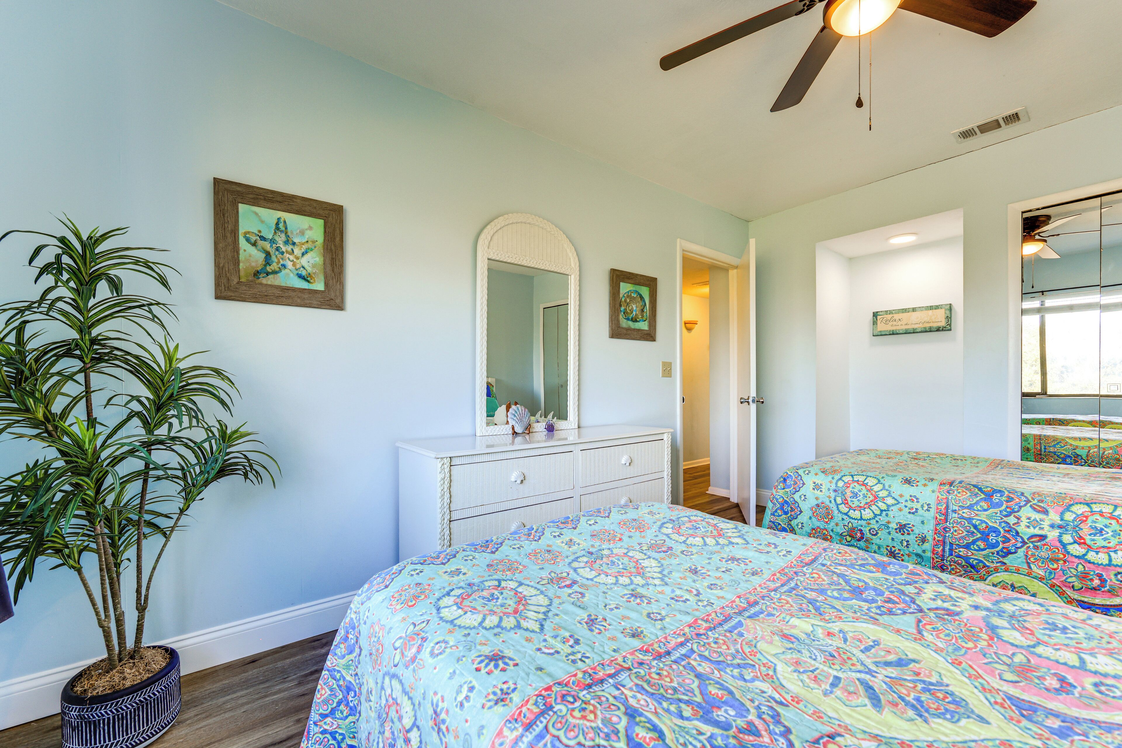 A bedroom with two beds, a dresser, a ceiling fan, and a potted plant.