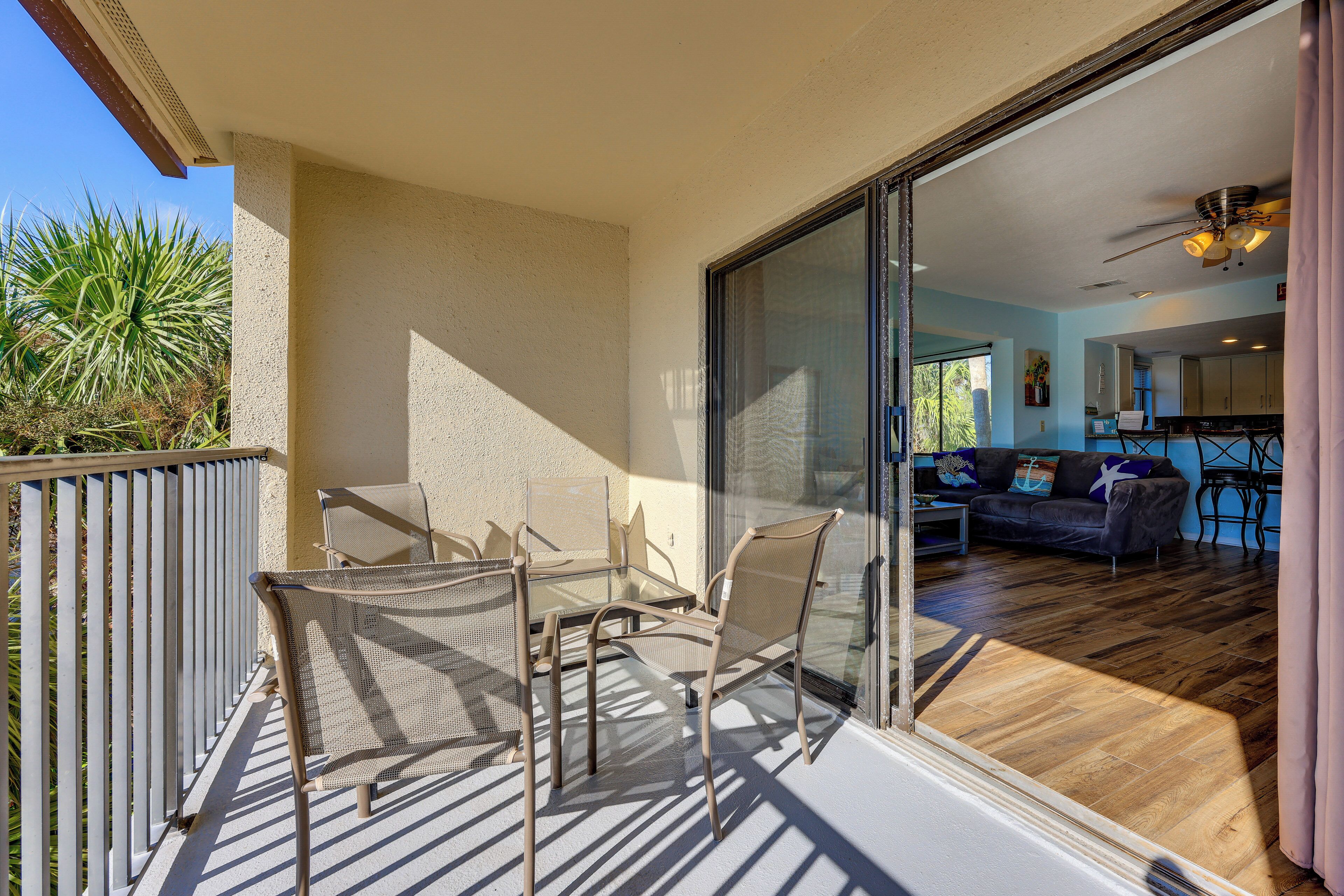 A balcony with a glass door leading to a living area, furnished with a table and chairs, and a view of a wooden floor and a couch.