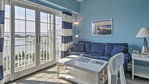 A room with a blue wall, a sofa, a coffee table, and a view of the water through large windows. - Walk to Beaches & Restaurants: Ocean City Condo (Ocean City)