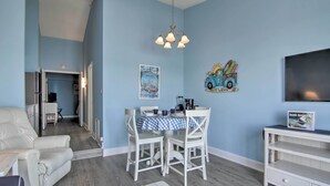 A room with a dining table, chairs, a white sofa, a TV, and a bookshelf. - Walk to Beaches & Restaurants: Ocean City Condo (Ocean City)