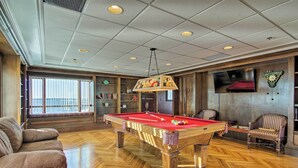 A pool table in a room with wooden flooring, a sofa, and a television mounted on the wall. - Walk to Beaches & Restaurants: Ocean City Condo (Ocean City)